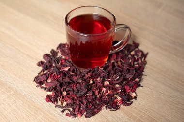 Bir fincan kırmızı çay ve ahşap bir masanın üzerinde çiçek.