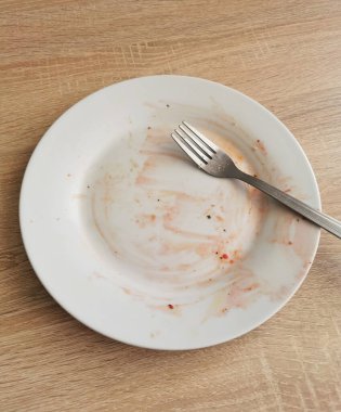 Ahşap masada yemekten sonra kirli boş tabak ve çatal.