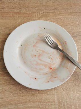 Ahşap masada yemekten sonra kirli boş tabak ve çatal.