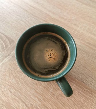 Tahta bir masanın üzerinde köpüklü yeşil kahve fincanı.