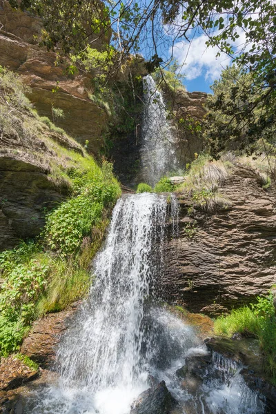 Sierra Nevada 'da bir vadide şelale, çimenler ve ağaçlar var, kayalar var ve gökyüzünde bulutlar var.