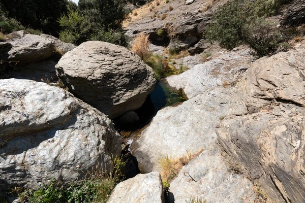 Sierra Nevada 'da bir vadiden akan su kayalık bir alandır, çimenler, çalılar ve ağaçlar vardır, gökyüzünde bulutlar vardır.