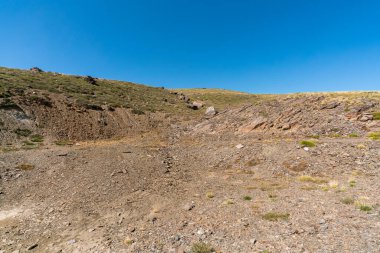 Sierra Nevada 'da aşınmış dağ yamacında, bitki örtüsü var, taşlar var ve gökyüzü açık.