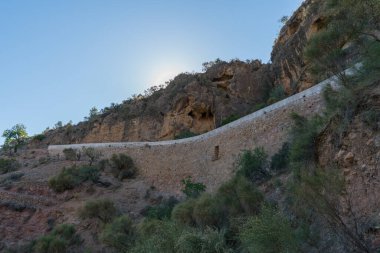İspanya 'nın güneyindeki dağlık arazi, taştan bir duvar var, çalılar ve ağaçlar var, gökyüzü açık.