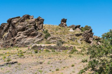 Sierra Nevada dağında kaya oluşumu, eski bir çiftlik evinin kalıntıları, ağaçlar, çalılar ve çimenler var.