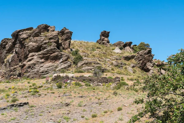 Sierra Nevada dağında kaya oluşumu, eski bir çiftlik evinin kalıntıları, ağaçlar, çalılar ve çimenler var.