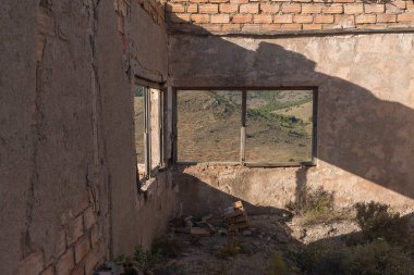 Eski bir maden kompleksinin içi tuğladan yapılmış, ahşap çerçeveli iki pencere var, bitki örtüsü var.