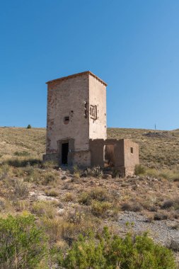Terk edilmiş bir maden tesisinde eski bir bina. Binanın iki kapısı var. Dağlık bir alan.
