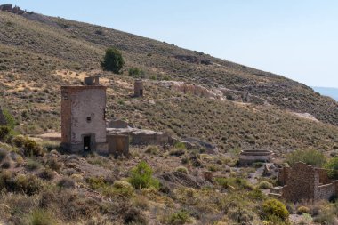 Eski ve terk edilmiş bir maden kompleksindeki bina, binanın pencere ve kapıları, binanın yanında çam ağaçları, dağlık bir alanda çam ormanı var.