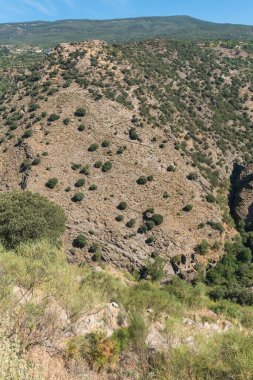 Sierra Nevada 'nın güneyindeki dağlık bölge, sarp bir bölge, ağaçlar ve çalılar var, harabeler var ve gökyüzü açık.