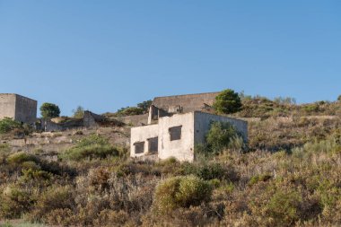 Terk edilmiş bir maden kompleksinde yıkılmış binalar, ağaçlar ve çalılar var, gökyüzü temiz.