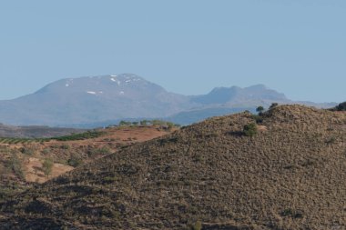 Güney İspanya 'nın dağlık bölgesi, ağaçlar ve çalılar var, dağlarda kar var, gökyüzü açık.