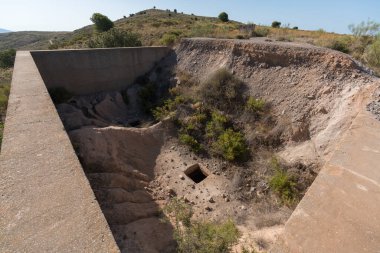 Terk edilmiş bir maden kompleksinin içinde zıpzıp betondan yapılmıştır, bitki örtüsü vardır, dağlık bir alandır ve gökyüzü temizdir.