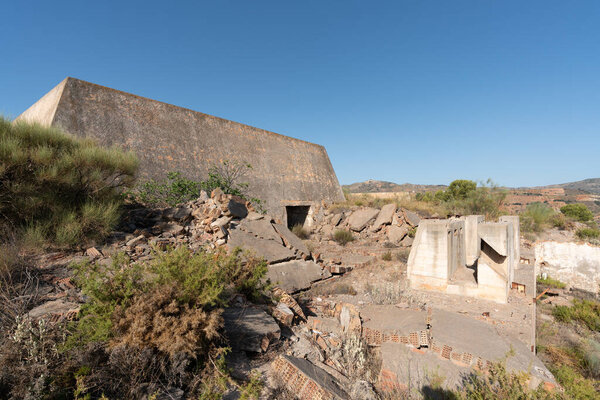 Construction in an abandoned mining complex in southern Spain, the construction is made of stone, brick and concrete, there are trees and shrubs, the sky is clear