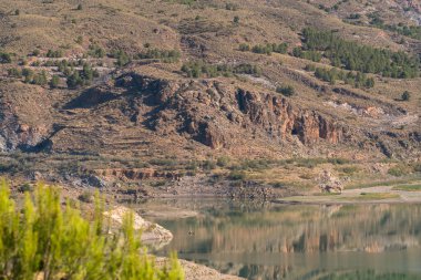 Güney İspanya 'daki Beninar Barajı' nda suda yansımalar var. Çam ağaçları ve çalılar var.