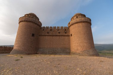 Güney İspanya 'daki La Calahorra Kalesi, kale taştan yapılmış, parmaklıklı birkaç pencere var, gökyüzünde bulut var.