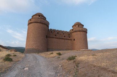 Güney İspanya 'daki La Calahorra Kalesi' ne giden toprak yol. Kalenin birkaç kulesi var, bitki örtüsü kuru ve gökyüzü bulutsuz.