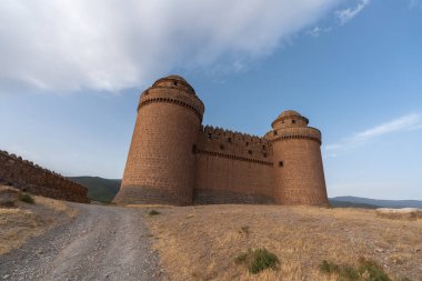 Güney İspanya 'da bir dağın tepesinde La Calahorra kalesi, kale taştan yapılmış, 2 kulesi var, çimenler kuru, gökyüzü bulutlu.