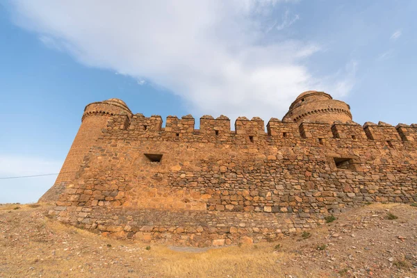 Güney İspanya 'da bir kalenin taş duvarı, duvarın birkaç penceresi var, kuru bitki örtüsü var, gökyüzünde bulut var.