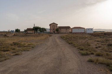 Güney İspanya 'daki La Calahorra tren istasyonunda toprak bir yol var, çalılar ve ağaçlar var, gökyüzü açık.