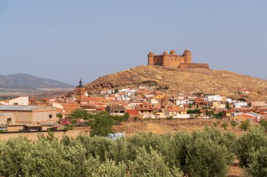 La Calahorra Kalesi bir dağın tepesinde, bir kasaba var, ağaçlar ve dağlar var, gökyüzü açık