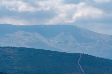 İspanya 'nın güneyindeki Sierra Nevada' nın dağlık arazisi. Çam ormanları, çimenler, gökte bulutlar var.