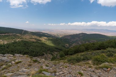İspanya 'nın güneyindeki Sierra Nevada' nın dağlık arazisi. Çam ormanları var, çimenler kuru, gökyüzünde bulutlar var.