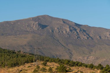 Güney İspanya 'da Sierra Nevada' da gün doğumu, bir çam ormanı var, yüksek voltaj hattı geçiyor, yamaçta kayalar var ve gökyüzü açık.