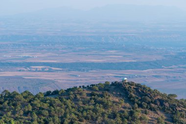 Sierra Nevada 'da bir dağın tepesindeki korucu evinde ağaçlar ve kayalar var. Binaların olduğu bir ova var.