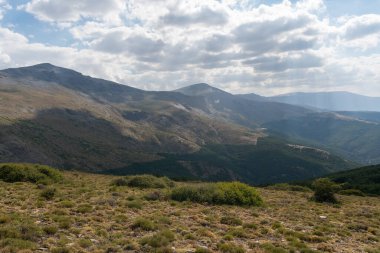 Güney İspanya 'da Sierra Nevada' nın dağlık arazisi, çam ormanı, çalılar ve çimenler, taşlar ve kayalar var, gökyüzünde bulutlar var.