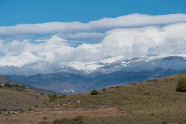 Güney İspanya 'daki Sierra Nevada' nın dağlık arazisi, dağ karlı, bitki örtüsü var ve gökyüzünde bulutlar var.
