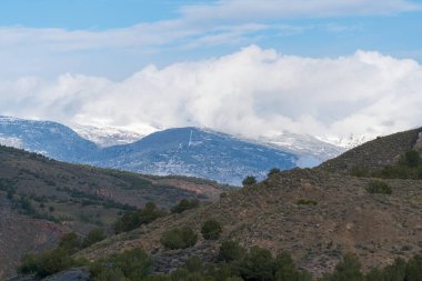Güney İspanya 'daki Sierra Nevada' nın dağlık arazisi, dağ karlı, bitki örtüsü var ve gökyüzünde bulutlar var.