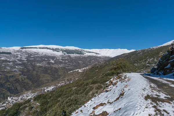 Sierra Nevada karla kaplı, ağaçlar ve çalılar var, birkaç köy var, kayalardan oluşan sarp bir bölge, gökyüzü açık.