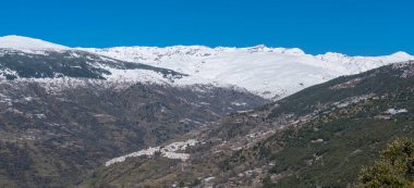 Sierra Nevada karla kaplı, ağaçlar ve çalılar var, birkaç köy var, gökyüzü açık.