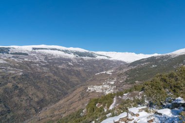 Sierra Nevada karla kaplı, ağaçlar ve çalılar var, birkaç köy var, gökyüzü açık.