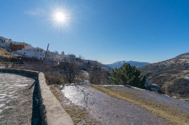 Sierra Nevada dağının yamacındaki Capileira kasabası sarp bir alandır. Bitkiler ve ağaçlar vardır. Kar vardır ve gökyüzü açıktır..