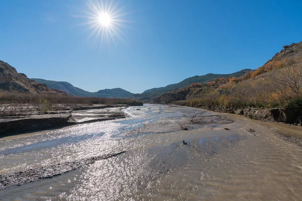 Güney İspanya 'daki Beninar rezervuarına doğru akan su nehri, dağlar ve ağaçlar var, taşlar var ve gökyüzü açık.