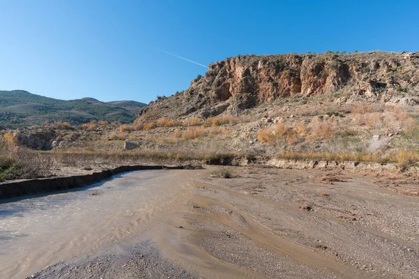 Güney İspanya 'daki Beninar rezervuarına doğru akan su nehri, dağlar ve ağaçlar var, taşlar var ve gökyüzü açık.