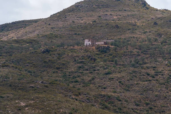 Güney İspanya 'daki eski çiftlik evi, çalılar ve ağaçlar var, kayalar var, gökyüzü bulutlu.