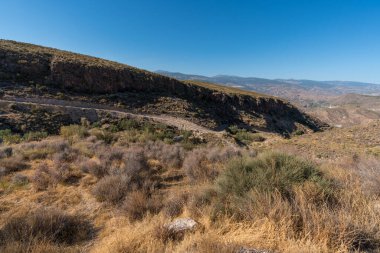 Güney İspanya 'da La Alpujarra' nın dağlık arazisi, ağaçlar ve çalılar var, gökyüzü açık.