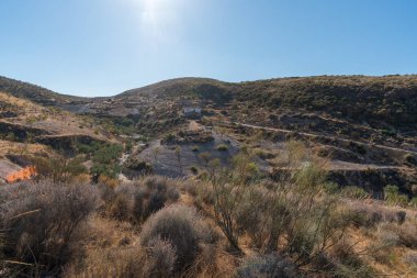 Güney İspanya 'da La Alpujarra' nın dağlık arazisi, ağaçlar ve çalılar var, harabeler içinde bir çiftlik evi var, gökyüzü açık.