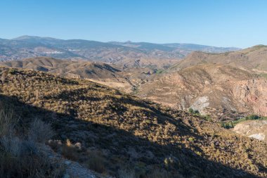 Güney İspanya 'da La Alpujarra' nın dağlık arazisi, ağaçlar ve çalılar var, gökyüzü açık.