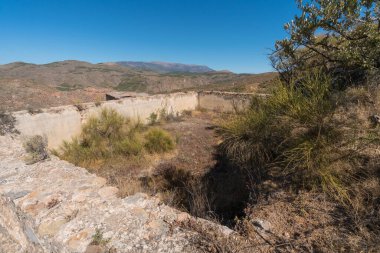 İspanya 'nın güneyindeki dağlarda eski bir havuz, havuz taş ve harç üzerine inşa edilmiş, çalılar ve ağaçlar var, dağlar var ve gökyüzü açık.