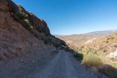 İspanya 'nın güneyindeki dağlarda toprak yol, çalılar ve ağaçlar, taşlar ve kaya geçidi var, dağlık bir bölge ve gökyüzü açık.