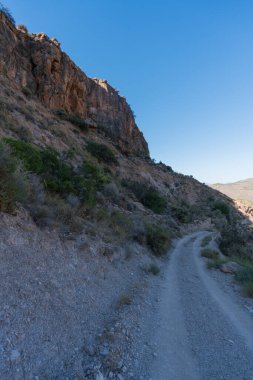 İspanya 'nın güneyindeki dağlarda toprak yol, çalılar ve ağaçlar, taşlar ve kaya geçidi var, dağlık bir bölge ve gökyüzü açık.