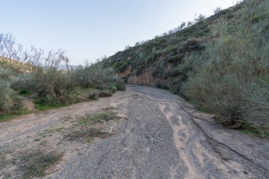 İspanya 'nın güneyinde küçük kuru bir dere, bir dağ bölgesi, çalılar, çimenler ve ağaçlar var, gökyüzü temiz.