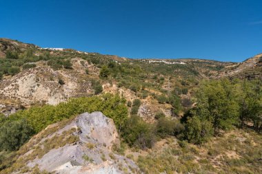 Güney İspanya 'nın dağlık bölgelerinde ağaçlar ve çalılar var. Dağ yamacında iki köy var. Gökyüzü açık.