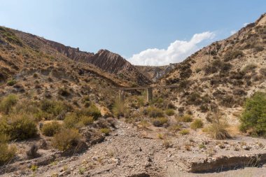 Güney İspanya 'da dağlık ve aşınmış bir manzara var, vadiyi geçen bir su kemeri var, kuru bir vadi var, bitki örtüsü var ve gökyüzü bulutlu.