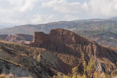 Güney İspanya 'da dağlık ve aşınmış bir arazi, bitki örtüsü var, dağ yamacında bir köy var, gökyüzü bulutlu.