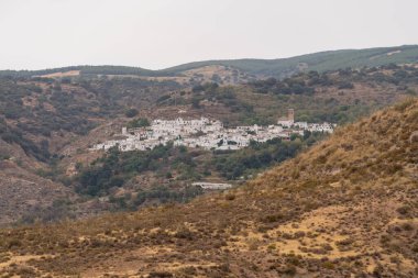 Sierra Nevada 'da bir dağın eteklerindeki kasabalar, beyaza boyanmış evlerinin cepheleri, bitkiler ve ağaçlar, gökyüzü bulutlu.